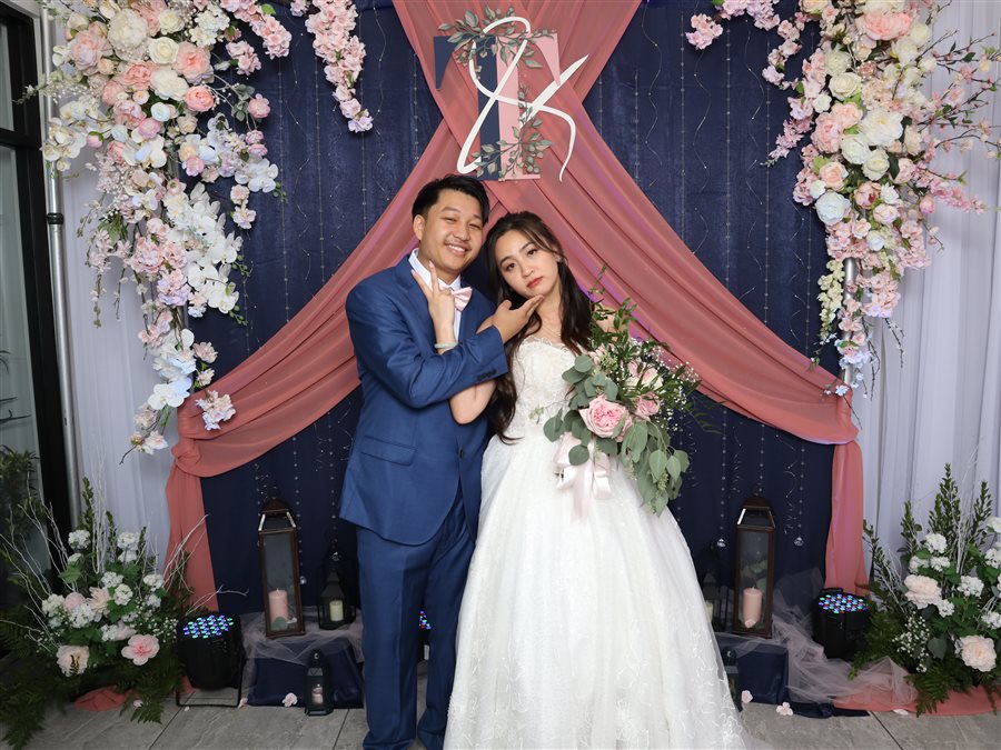 Bride and groom posing in front of a floral wedding arch photo booth backdrop